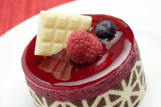 Delicious raspberry mousse pastry with fruit and white chocolate trimmings.  The focus of the photo is on the raspberry and the front of the pastry.